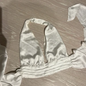 Vit topp från Zara - Vit halterneck topp från Zara i ett sidenliknande material. Toppen har en knytning i ryggen och en djup urringning framtill. Perfekt för fest eller i sommar!! Har lite missfärgning och lite trådar som gått upp men inget man tänker på!⭐️ Storlek M men passar S