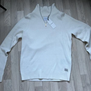 Vit stickad tröja från Jack & Jones - Säljer en stilren vit stickad tröja från Jack & Jones med halv zip. Perfekt för vintern eller lite kyligare dagar, har aldrig använt då den är för stor. Den är stor i storleken 