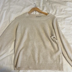 Beige stickad tröja från Vero Moda - Mysig beige stickad tröja från Vero Moda. Perfekt för kyliga dagar med sin mjuka och bekväma passform. Tröjan har långa ärmar och ribbade kanter vid ärmslut och nederkant.