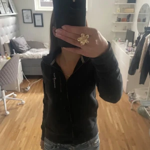 Sail racing kofta - Säljer en svart hoodie från Sail racing med dragkedja framtill. Tröjan har långa ärmar och en praktisk huva. Väldigt trendig. Dragkedjs grejen har gått av men går säkert att fixa 