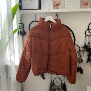 Orange pufferjacka med dragkedja - Snygg orange pufferjacka med hög krage och dragkedja framtill. Perfekt för kyligare dagar med sin vadderade design. Jackan har långa ärmar och en modern look. Jackan har några defekter därav billiga priset! 