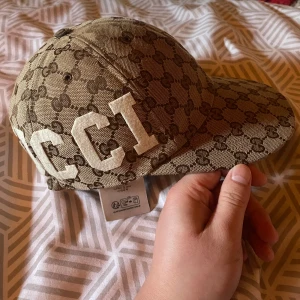 Gucci keps med logotypmönster - Snygg beige keps från Gucci med det ikoniska logotypmönstret i brunt. Kepsen har stora vita bokstäver och siffror på sidorna.                                   Är även intresserad för byte mot en likadan/annan gucci keps fast i storlek s/m!  Pris inte hugget i sten men inga skambud