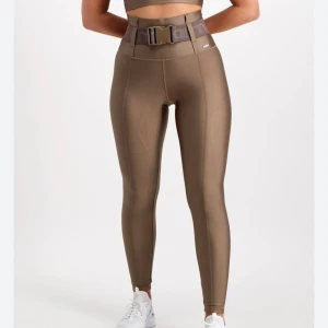 Bruna leggings med bälte - Snygga bruna leggings med hög midja och ett coolt bälte i midjan. Perfekta för en trendig look, oavsett om du är på språng eller bara vill känna dig bekväm. Helt oanvända och bälte medföljer 