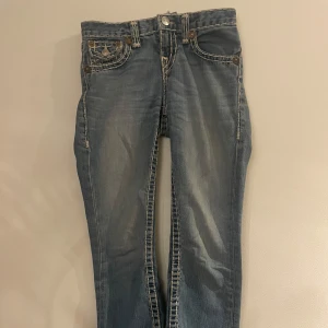 Bootcut true religion jeans - Säljer ett par klassiska blå jeans från True Religion med snygga kontrastsömmar och femficksdesign. Jeansen har en knappgylf och är i en avslappnad passform. Perfekta för en cool och avslappnad stil. Skriv gärna om ni har frågor!