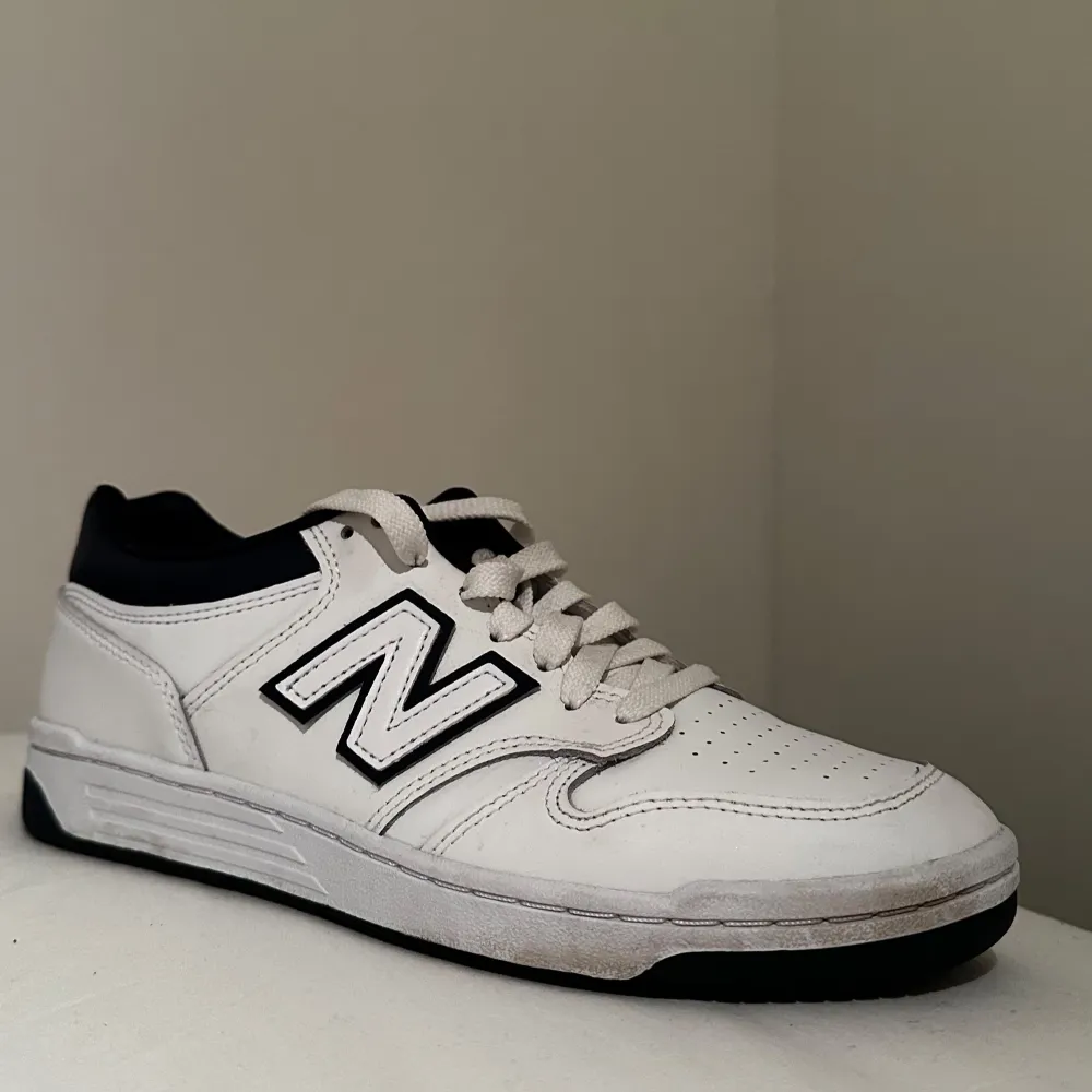 Snygga vita sneakers från New Balance med mörkblå detaljering och snörning. Perfekta för en casual look med sin klassiska design och bekväma passform.. Kengät.