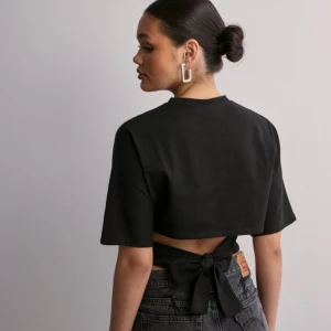 Svart croppad topp med knyt - Snygg svart croppad topp med korta ärmar och knytning i ryggen. Perfekt för en trendig look. Säljer pågrund av att den ej kommit till användning så därför i väldigt bra skick.