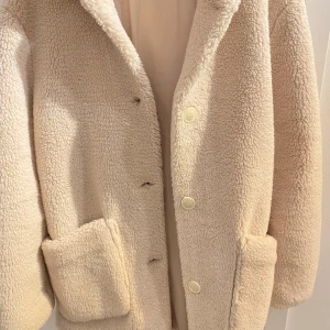 Beige teddyjacka från H&M - Mysig beige teddyjacka från H&M med knappar framtill. Perfekt för kyliga dagar med sin fluffiga och varma design. Jackan har långa ärmar och två praktiska fickor.