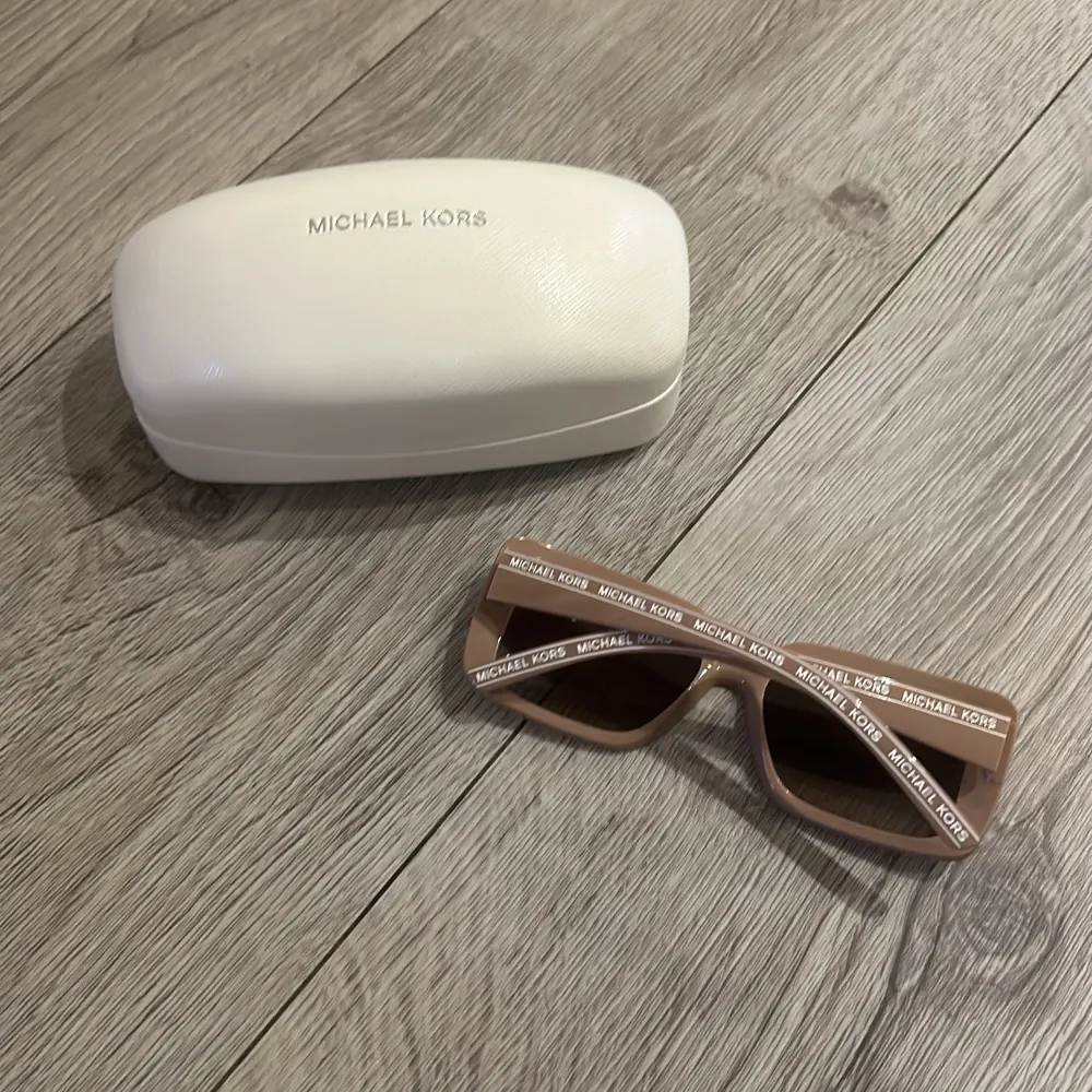 Snygga solglasögon från Michael Kors i en trendig beige/ rosa färg. De har en fyrkantig form och logotypen tryckt på bågarna. Perfekta för att ge en stilren touch till din look. Kommer med ett vitt fodral för säker förvaring.. Asusteet.