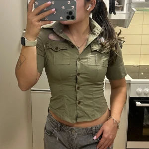 Kortärmad topp med broderier - UNIK figursydd topp/skjorta, sitter tajt och pushar verkligen upp brösten. Toppen har coola broderade detaljer samt små nitar vid fickorna. Köpt på unik pop-up secondhandbutik (Vinokilo) i Stockholm ! Kan diskutera pris💗 