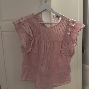 Rosa blus från & Other Stories - Söt rosa blus från & Other Stories med vackra spetsdetaljer och volanger på ärmarna. Perfekt för alla tillfällen. Blusen har en rund hals och är i ett jätteskönt material.
