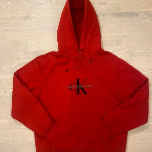 Röd hoodie från Calvin Klein Jeans - Säljer en snygg röd hoodie från Calvin Klein Jeans med klassisk logga på bröstet. Den har en justerbar huva och en praktisk magficka. Perfekt för en avslappnad stil och den är tjock så passar perfekt nu på vintern .Nästan aldrig använd och är i storlek L. Inga fläckar eller hål. Priset kan såklart diskuteras☺️