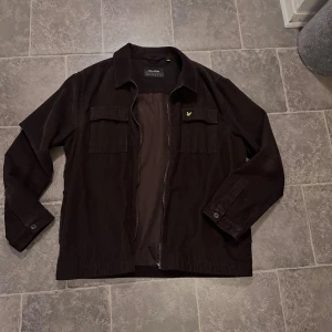 Lyle & Scott jacka  - En tunn Lyle & Scott jacka med dragkedja i färgen brun, och i ett tyg som liknar mocka. Storleken är L och skicket är 9/10! Passar perfekt till hösten och våren! Säljs för 500 kr!
