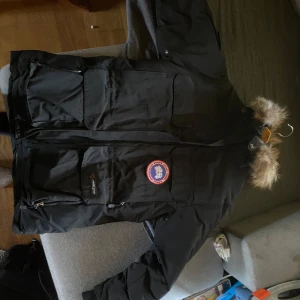 Svart Canada Goose Jacka - Säljer en svart jacka från Canada Goose. Jackan har en pälsfodrad huva och flera praktiska fickor. Perfekt för kalla vinterdagar. Den är i bra skick och redo för nya äventyr! Det är storlek S på den men den passa mig och jag har storlek M/L på jackor