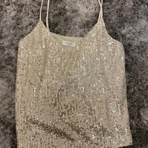 Glittrig beige paljettopp från Stockh LM Studio - Säljer en superfin glittrig topp från Stockh LM Studio i storlek XS. Den är beige med massor av paljetter som verkligen fångar ljuset. Perfekt för festliga tillfällen! Toppen har smala axelband och en v-ringad design. Den är i nyskick och redo för att bli din nya favorit i garderoben! ✨
