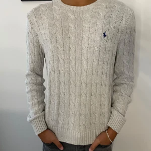 Kabelstickad Ralph Lauren Tröja Grå - Säljer denna feta gråa kabelstickade tröja från Ralph Lauren. Den är i väldigt gott skick och sparsamt använd. Nypris på denna ligger på över 2000, mitt pris ligger endast på 600. Tveka inte på att höra av dig vid fler frågor eller funderingar!