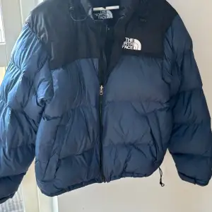 1996 Retro Nuptse JacketSäljer en snygg och varm pufferjacka från The North Face i blått och svart. Fodrad med RDS-certifierat dun - en certifiering som säkerställer en ansvarsfull djurvälfärd och hantering av dun samt fjädrar. Fyllnadsgrad: 700 