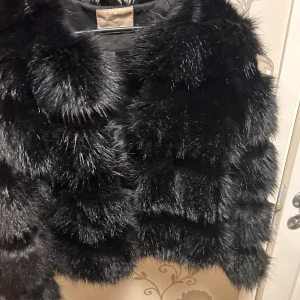 Svart pälsjacka - Säljer en superfluffig och snygg svart pälsjacka. Perfekt för att hålla sig varm och stilren under kyliga dagar. Jackan har långa ärmar och en lyxig känsla. Passar perfekt för både vardag och fest!