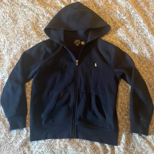 Ralph lauren zip hoodie - En fet mörkblå Ralph lauren hoodie med ett vitt Raffe märke!🙌 8/10 skick förutom defekter på båda ärsmlutarna! men inget stort som man tänker på! men kan vara bra att veta! 🙌 Bara att skicka till mig om det är något om den eller om storlek osv!🫡