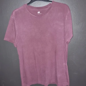 Vinröd t-shirt från H&M - Säljer en stilren vinröd t-shirt från H&M i storlek L. Den har en klassisk crewneck-design och är tillverkad i ett mjukt material som känns skönt mot huden. Perfekt för en avslappnad look. Den är solid och inte flammig som på bilderna.