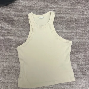 Beige ribbad linnetopp från Gina trico - Säljer en stilren beige ribbad linnetopp från Gina trico. Perfekt för varma dagar med sin ärmlösa design och mjuka material. Toppen har en klassisk rund halsringning och är i en neutral färg som passar till det mesta.