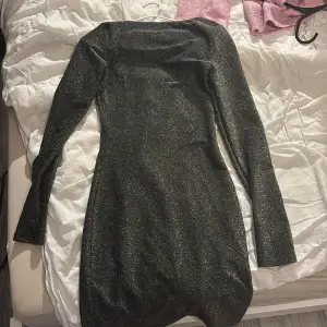 Snygg svart glittrig klänning med långärmad design och en djup v-ringning. Perfekt för en kväll ute eller en festlig tillställning. Klänningen har en tight passform som framhäver figuren.