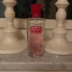 Madonna Daydream Eau de Toilette - Säljer en Madonna Daydream Eau de Toilette med en elegant glasflaska i rosa nyans. Flaskan har en röd kork och en stilren design som passar perfekt på sminkbordet. Perfekt för den som vill ha en fräsch och feminin doft.