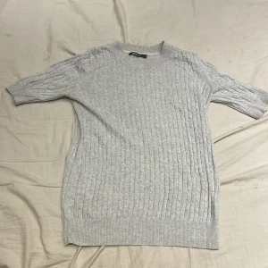 Grå t-shirt från Gina Tricot - Säljer en stilren grå t-shirt från Gina Tricot. Tröjan har ett klassiskt flätmönster och korta ärmar, perfekt för lager-på-lager eller som den är.❤️