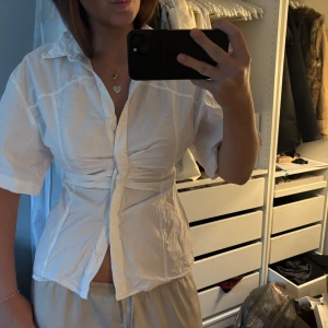 Vit kortärmad blus med midja - Stilren vit blus med korta ärmar. Blusen har knappar framtill och en krage. 