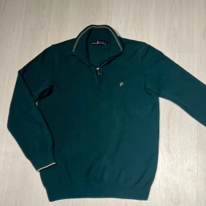 Grön denim culture quarter zip - Snygg grön tröja från denim culture med dragkedja vid halsen och ett litet broderat emblem på bröstet. Tröjan har långa ärmar och ribbade muddar vid ärmslut och nederkant. Perfekt för en stilren look. Storlek M