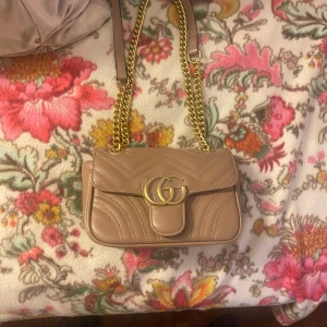 Beige axelväska med gulddetaljer - Snygg beige axelväska i skinn med quiltad design och guldfärgad kedja. Väskan har ett stort GG-emblem. Oanvänd 