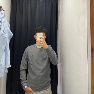 Grå Ralph lauren tröja  - Säljer en stilren grå tröja från Ralph Lauren med v-ringning. Tröjan har långa ärmar och en liten broderad logotyp på bröstet. Perfekt för en avslappnad men snygg look.