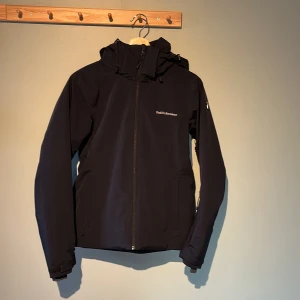 Svart jacka från Peak Performance - Snygg svart jacka från Peak Performance med dragkedja och huva. Perfekt för kyligare dagar med sin quiltade insida. Jackan har långa ärmar och en stilren design med logotypdetaljer på bröstet och ärmen. Det är en fodrad skidjacka med snölås. Helt oanvänd bara testad😁 Pris går såklart att diskutera🤝
