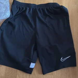 Svarta shorts från Nike - Snygga svarta shorts från Nike med elastisk midja och det klassiska Nike-logotypen i vitt. Perfekta för sport och träning. Storlek XL för 158-170cm