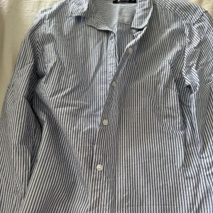 Randig skjorta från Gina trickot - Snygg blå- och vitrandig skjorta från Gina trickot. Perfekt för en stilren look med knappar framtill och klassisk krage. Skjortan har långa ärmar och är gjord i ett bekvämt bomullsmaterial.