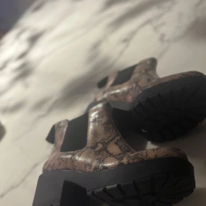 Ormmönstrade chelsea boots - Snygga chelsea boots med ormmönster och robust klack. Skorna har elastiska paneler på sidorna för enkel på- och avtagning. Perfekta för att ge din outfit en edgy touch.