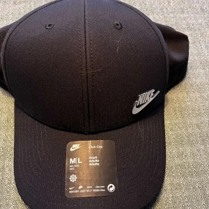 Svart keps från Nike - Säljer en stilren svart keps från Nike i storlek M/L. Kepsen har en klassisk design med Nike-loggan i metall på framsidan. Perfekt för både vardag och sportiga aktiviteter. Köpt i Nederländerna men äkta såklart. Nyskick aldrig använd då jag fick den i present men inte tyckte om den… storleken går att justera. Vid frågor skriv, mvh Maxi