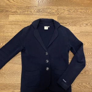 Mörkblå kavaj från Boomerang  - Snygg mörkblå kavaj från Boomerang med tre knappar framtill och två fickor. Perfekt för en stilren look. Kavajen har långa ärmar och en klassisk krage.