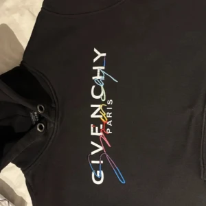 Givenchy hoodie - Snygg svart hoodie från Givenchy med färgglad logotyp på bröstet. Perfekt för en stilren och modern look. Hoodien har en klassisk passform med dragsko i huvan.
