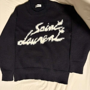 Svart tröja från Saint Laurent - Snygg svart tröja från Saint Laurent med vit text på framsidan. Tröjan har en klassisk rund halsringning och långa ärmar. Perfekt för en stilren look.