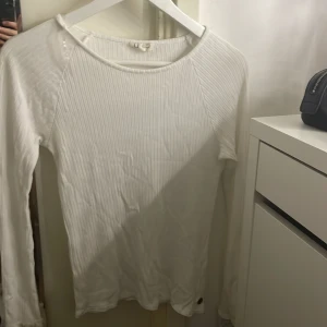 Vit ribbad långärmad tröja från Ü - Säljer en stilren vit ribbad tröja från Ü med långa ärmar. Perfekt för en avslappnad look. Tröjan har en rund halsringning och är tillverkad i ett mjukt material.