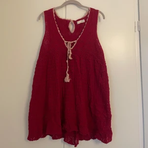 Söt topp från Odd Molly - Charmig röd tröja från Odd Molly med vackert spetsmönster och knytning framtill. Den är ärmlös och har en luftig passform, perfekt för varma dagar. Den dekorativa kanten och knytningen ger en bohemisk touch.