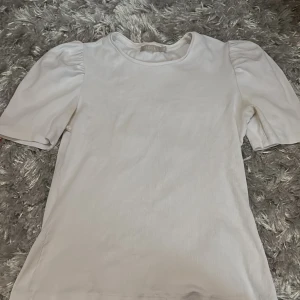 Vit ribbad topp från Pieces - Säljer en vit T-shirt med puffarmar.Storlek M men är liten i storlek så passar till mindre storlekar med🩷
