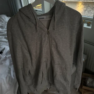 Grå hoodie från Weekday - Säljer en stilren grå hoodie från Weekday med dragkedja och huva. Perfekt för en avslappnad look. Den har långa ärmar och är tillverkad i mjukt material för extra komfort. Tror storleken är herr M