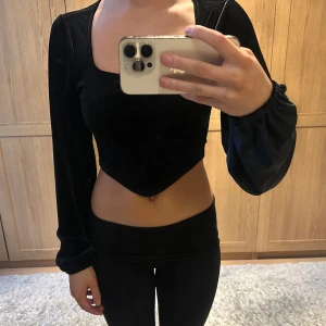 Svart sammetstopp - Snygg svart sammetstopp med lång ärm och en croppad design. Toppen har en elegant fyrkantig urringning och är perfekt för en trendig look.
