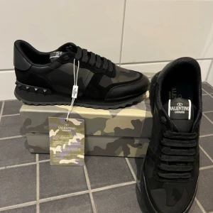 Svarta Valentino Rockrunners - Snygga svarta Valentino Garavani sneakers med kamouflagemönster och nitar på sulan. Skorna har snörning och en stilren design som passar perfekt för den stiliga vintern. Allt kommer med!!