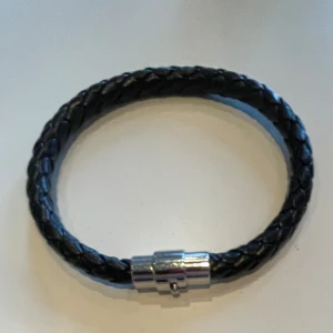 Svart flätat armband med metallspänne - Snyggt svart flätat armband med ett stilrent metallspänne. Perfekt accessoar för en cool och avslappnad stil. Passar både till vardags och speciella tillfällen.