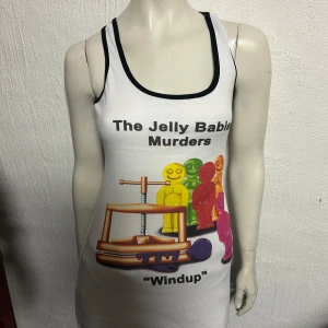 Vit linneklänning med tryck - Säljer en vit linneklänning med ett humoristiskt tryck av färgglada figurer och texten 'The Jelly Babies Murders'. Klänningen har svarta kanter vid ärmhålen och halsringningen. Perfekt för en avslappnad och rolig stil.