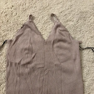 Beige ribbad topp från Divided - Säljer en snygg beige ribbad topp från Divided. Toppen har smala axelband och en v-ringad design med knytning i ryggen. Perfekt för en stilren look!