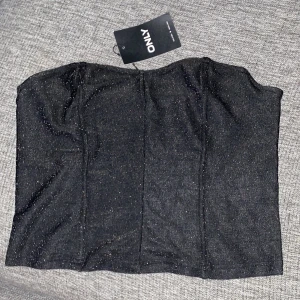 Svart glittrig tubtopp från ONLY - Snygg svart tubtopp från ONLY med glittrande detaljer. Perfekt för en kväll ute eller festliga tillfällen. Enkel och stilren design som passar till många outfits.