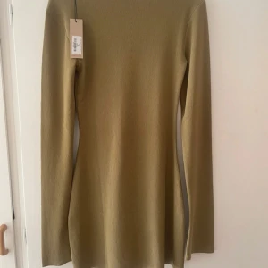 Olivgrön långärmad klänning från ADSGN - Snygg olivgrön klänning från ADSGN med lång stretchig passform. Perfekt för en stilren look med sin enkla design och långa ärmar. Klänningen är tillverkad i ett ribbat material som ger en bekväm känsla. Passar utmärkt för både vardag och speciella tillfällen.